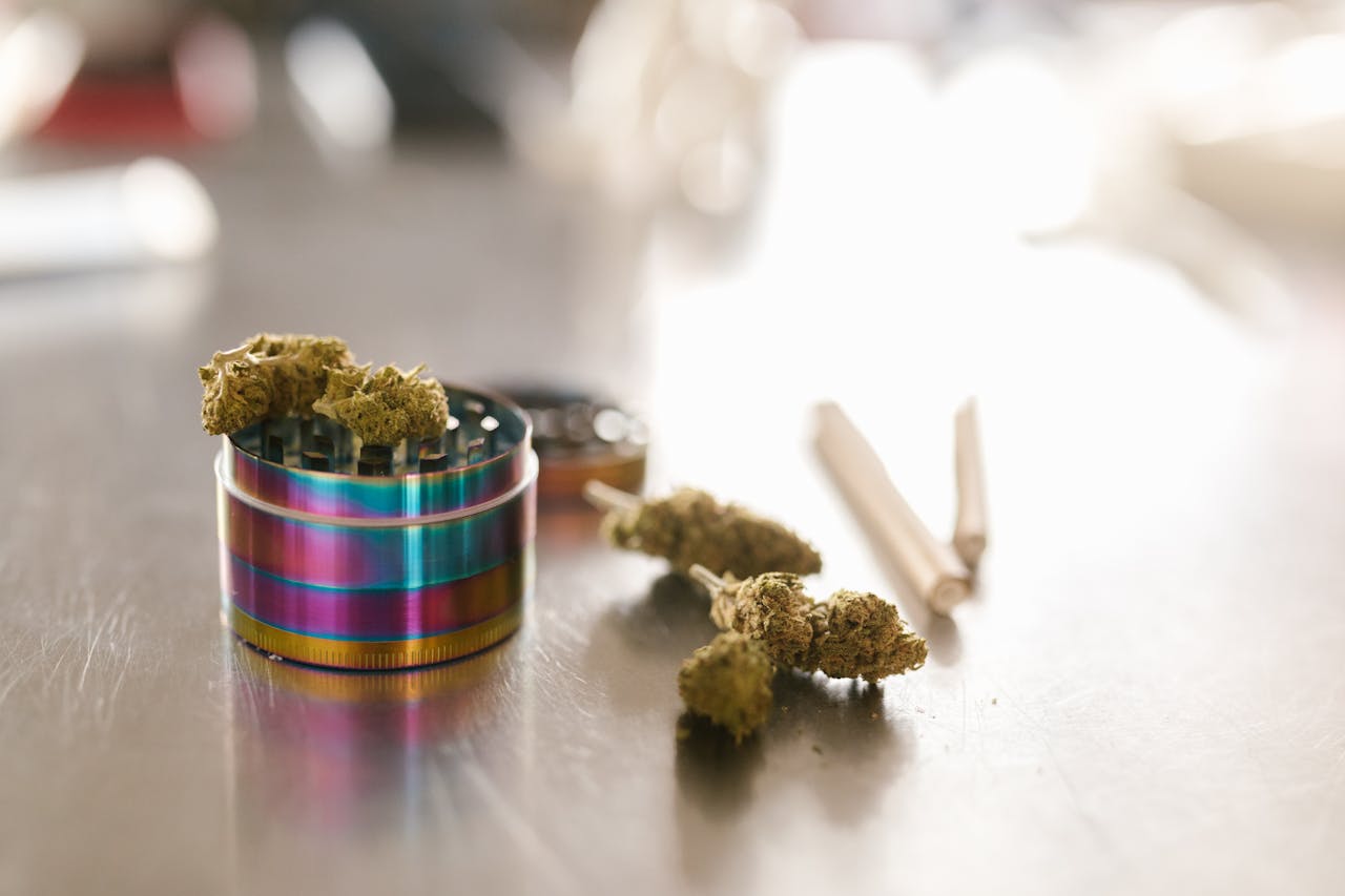 services-01 Cannabis buds with a colorful grinder on a reflective surface in natural light.